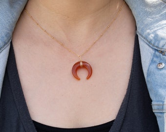May include: A gold chain necklace with a carnelian crescent moon pendant.