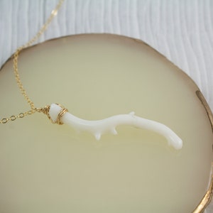 Puede incluir: Un delicado collar de cadena dorada con un colgante de rama de coral blanco. La rama est&aacute; envuelta en alambre dorado y tiene una forma natural y org&aacute;nica.