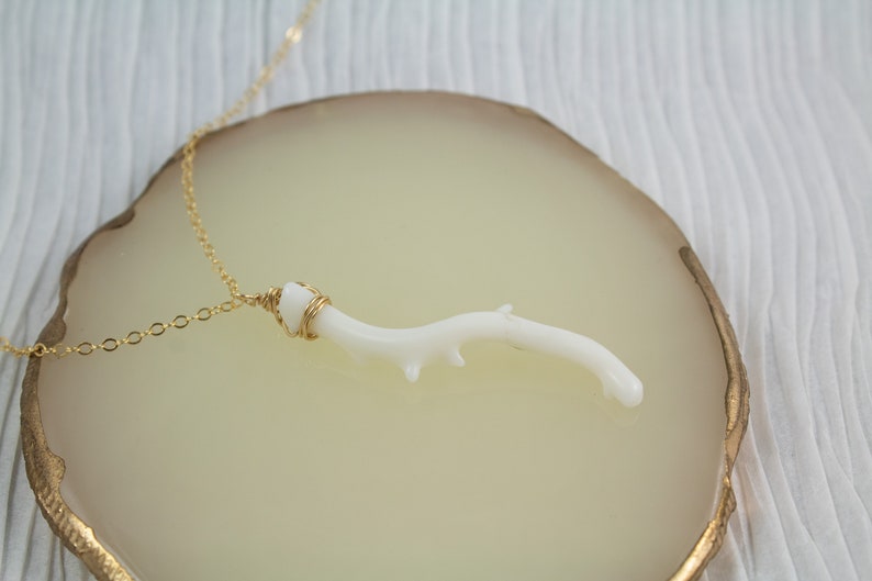 Puede incluir: Un delicado collar de cadena dorada con un colgante de rama de coral blanco. La rama est&aacute; envuelta en alambre dorado y tiene una forma natural y org&aacute;nica.