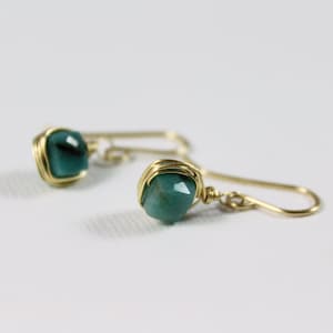 May include: A pair of gold wire wrapped earrings with green gemstone accents.