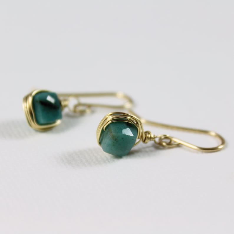 May include: A pair of gold wire wrapped earrings with green gemstone accents.