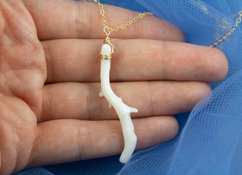 Puede incluir: Un delicado collar de cadena dorada con un colgante de rama de coral blanco. La rama de coral est&aacute; envuelta en alambre dorado y tiene una forma natural y org&aacute;nica.