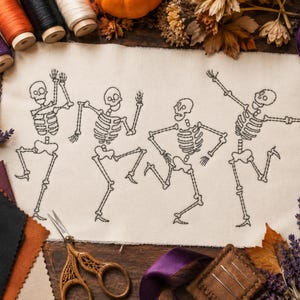 Pode incluir: Uma peça retangular de tecido branco sujo com um design bordado a preto de quatro esqueletos em várias poses de dança. Os esqueletos são representados com linhas simples, mostrando caixas torácicas, crânios e membros em movimento.