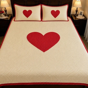 May include: A cream-colored bedspread and two matching pillowcases featuring a textured, waffle-knit pattern. Each piece is accented with a large, solid red heart in the center and finished with a vibrant red border along the edges.