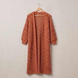May include: A long, open-front cardigan in a burnt orange hue, featuring an intricate, repeating crochet lace pattern throughout the body and sleeves. The garment has long sleeves with ribbed cuffs and a straight, floor-length hemline.