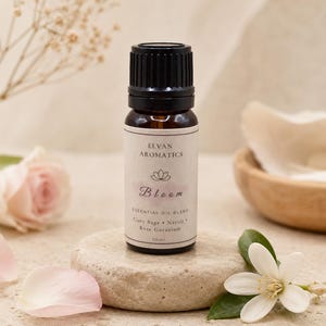 May include: A 10ml amber glass essential oil bottle with a black cap and a white label reading Elvan Aromatics Bloom Essential Oil Blend, Clary Sage, Neroli, Rose Geranium. The bottle is centred on a round, light-coloured stone surface.