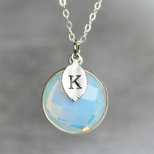 May include: A silver necklace with a blue opal pendant and a silver leaf charm with the letter K engraved on it.