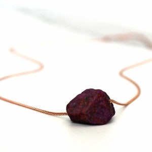 May include: A rose gold chain necklace with a large, raw ruby pendant.