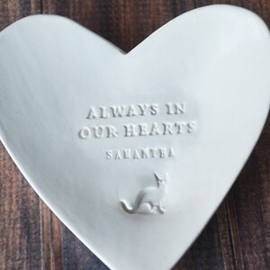 White ceramic heart-shaped dish with the text "Always in our hearts Samantha" and a small cat silhouette.