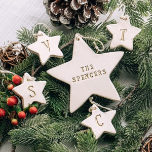 Five white ceramic star ornaments. The ornaments are personalized with the family name and first initials on separate ornaments.