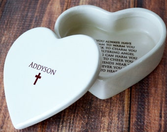 May include: A white heart-shaped ceramic trinket box with a removable lid. The lid features the name ADDYSON above a brown cross. The interior base of the box contains printed text that reads: YOU ALWAYS HAVE A DREAM TO WARM YOU, A WISH TO CHARM YOU, A SHELTERING ANGEL SO NOTHING CAN HARM YOU, A RAINBOW TO CHEER YOU, AND FRIENDS NEAR YOU, AND WHENEVER YOU PRAY, YOU ARE NEAR TO HEAVEN.