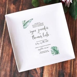 White wedding invitation imprinted on a square ceramic plate. The invitation is personalized to the special couple's big day.