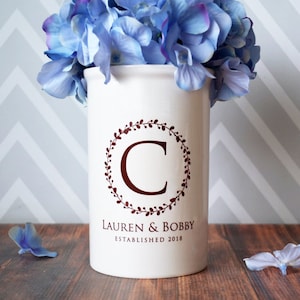 May include: White ceramic vase with a brown floral wreath and the letter C in the center. The vase also has the text "Lauren & Bobby Established 2018".