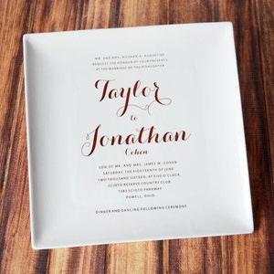 May include: A white ceramic plate with a wedding announcement for Taylor and Jonathan Cohen. The announcement includes the date, time, and location of the wedding ceremony. The text is printed in black and red.