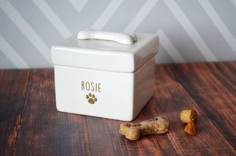 White ceramic dog treat jar with a bone-shaped lid. The jar has the name "Rosie" and a paw print in gold lettering.