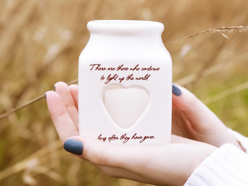 May include: White ceramic jar with a heart-shaped cutout and the text "There are those who continue to light up the world long after they have gone."