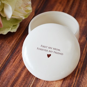 K&ouml;nnte beinhalten: Wei&szlig;e Keramik-Schmuckschatulle mit Deckel. Der Deckel tr&auml;gt den Text "First my mom, forever my friend" und ein kleines rotes Herz.