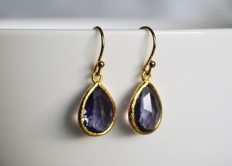 K&ouml;nnte beinhalten: Ein Paar goldene Ohrringe mit tropfenf&ouml;rmigen Amethyststeinen.