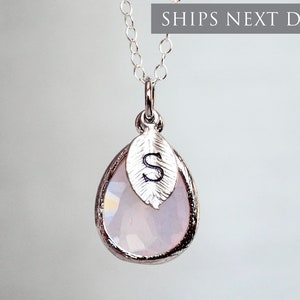 May include: A silver necklace with a teardrop-shaped pendant featuring a clear, iridescent stone and a silver leaf charm with the letter "S" engraved on it.