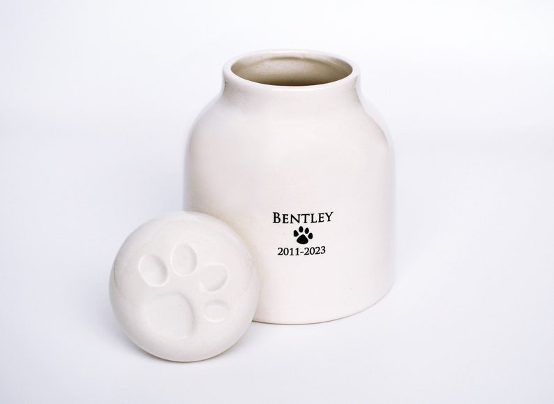 paw print imprint on lid of a white ceramic pet urn for dog ashes. Personalized