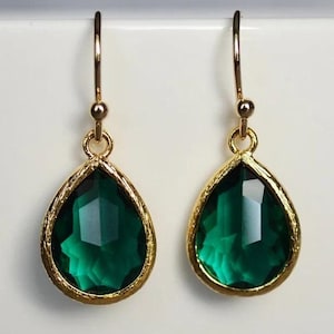 May include: A pair of gold teardrop earrings with emerald green glass stones.