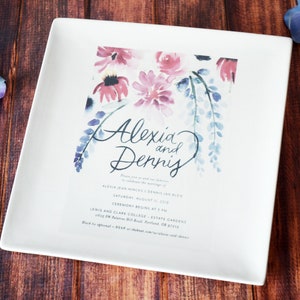 A large square serving plate sits on a wooden table. The plate has a full color custom image centered on the front. The image is a custom wedding invitation with flowers at the top and text. The plate is white with a gloss glaze finish.
