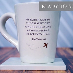 May include: White ceramic coffee mug with a quote by Jim Valvano: "My father gave me the greatest gift anyone could give another person. He believed in me." The quote is printed in purple and the mug has a small brown airplane graphic.