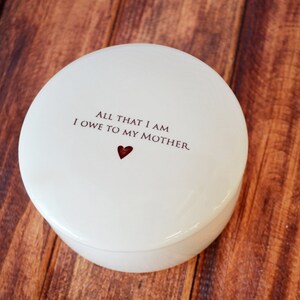 May include: White ceramic trinket box with a red heart and the text "All that I am I owe to my mother."