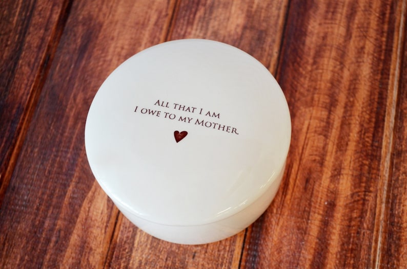 May include: White ceramic trinket box with a red heart and the text "All that I am I owe to my mother."