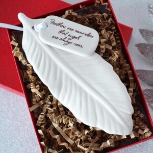 May include: White ceramic feather ornament with a tag that reads "Feathers are reminders that angels are always near."