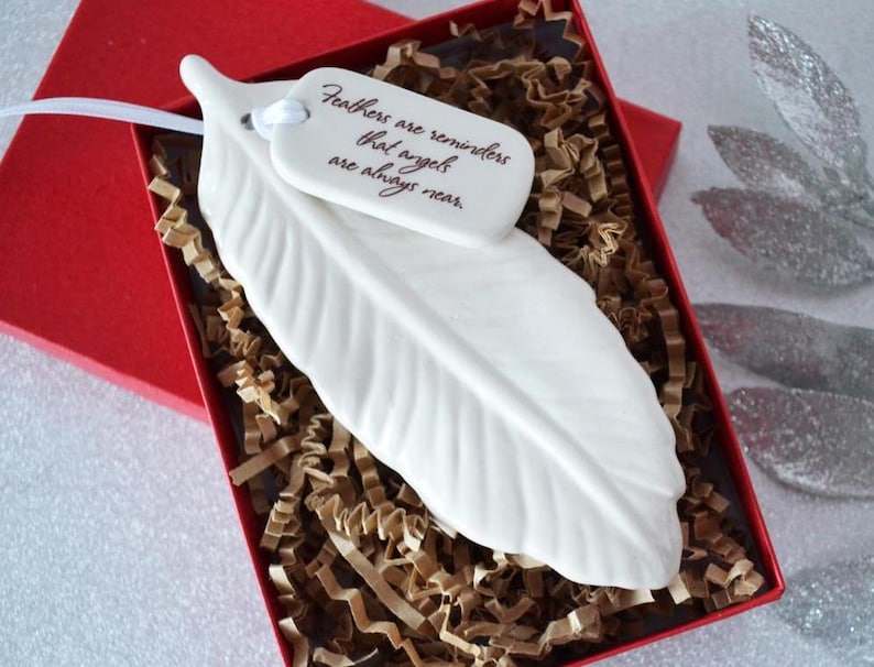 May include: White ceramic feather ornament with a tag that reads "Feathers are reminders that angels are always near."