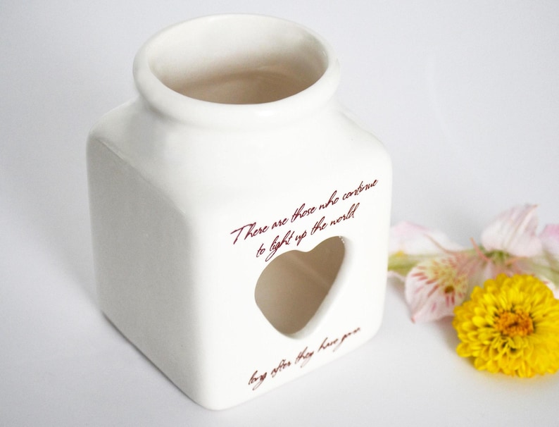 May include: White ceramic candle holder with a heart-shaped cutout and the quote "There are those who continue to light up the world, long after they have gone."