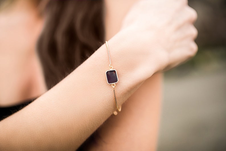 A gold chain bracelet with a square-shaped ruby gemstone.