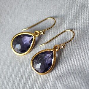 K&ouml;nnte beinhalten: Ein Paar goldene Tropfenohrringe mit violetten Edelstein-Akzenten.