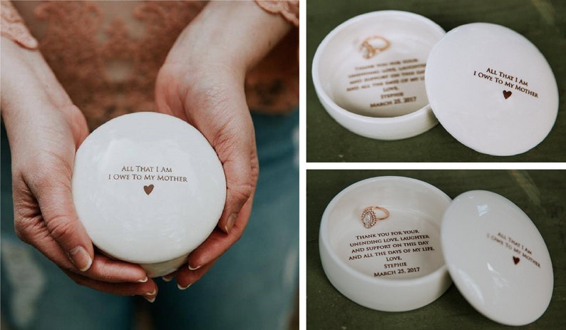 May include: A white ceramic ring box with a lid. The lid has the inscription "All that I am I owe to my mother" with a small heart symbol. The inside of the box has the inscription "Thank you for your unending love, laughter, and support on this day and all the days of my life. Love, Stephus, March 25, 2017". A gold ring is inside the box.
