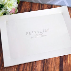 May include: A white framed print with the names "Nese & Ryan", the date "6.13.2014", and the location "Istanbul, Turkey" in gray lettering. The print is on a wooden surface with a bouquet of flowers in the upper left corner.