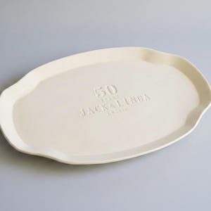 Ivory colored, handmade ceramic serving platter with an irregular, wavy edge. The platter is embossed with the text "50 YEARS JACK & LINDA 2.9.2026".  Anniversary gift.