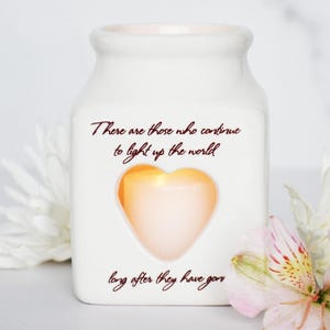 May include: White ceramic jar with a heart-shaped cutout and a quote that reads "There are those who continue to light up the world long after they have gone".