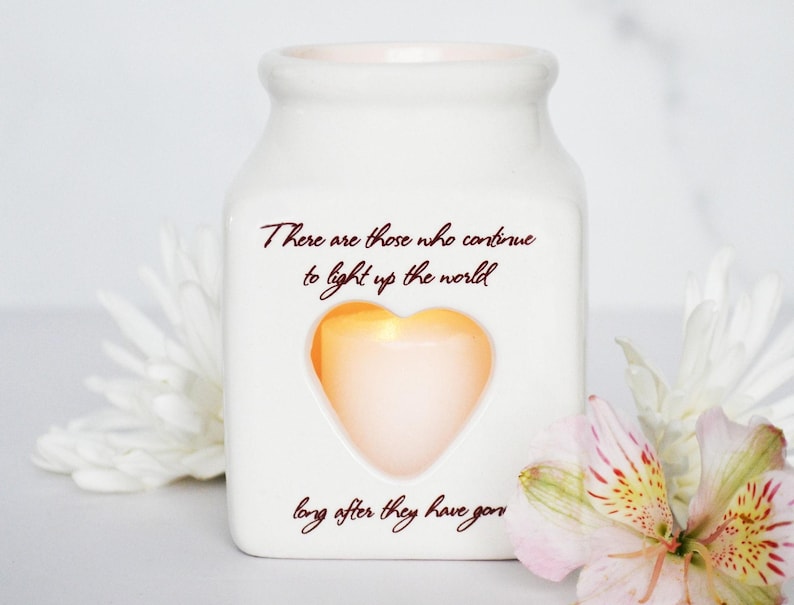 May include: White ceramic jar with a heart-shaped cutout and a quote that reads "There are those who continue to light up the world long after they have gone".
