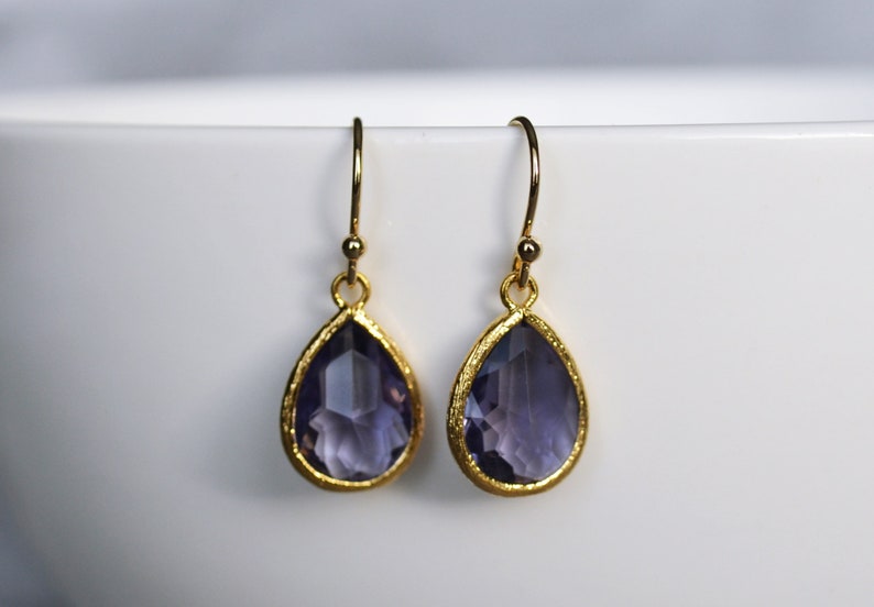 K&ouml;nnte beinhalten: Ein Paar goldene Ohrh&auml;nger mit tropfenf&ouml;rmigen Amethyststeinen.