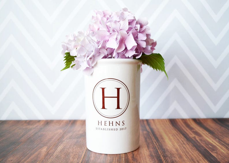 White ceramic vase with a monogram 'H' and the text 'Hehns Established 2017'. The vase is filled with pink flowers.