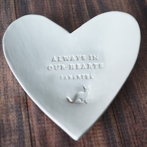 May include: White ceramic heart-shaped dish with the inscription "Always in our hearts Samantha" and a small cat silhouette.