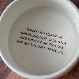 May include: White ceramic bowl with a brown inscription that reads "THANK YOU FOR YOUR UNENDING LOVE, LAUGHTER AND SUPPORT ON THIS DAY AND ALL THE DAYS OF MY LIFE."