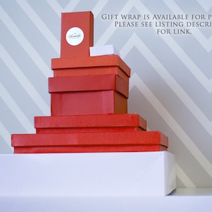 Informational image with directions on adding a gift box.  Shows a group of gift boxes of various sizes. Each is solid red or white with a metallic silver Susabella seal. Gift wrap is available for purchase. Please see listing description for link.