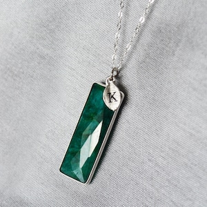 May include: A silver chain necklace with a rectangular green gemstone pendant and a small silver leaf charm with the letter 'K' engraved on it.