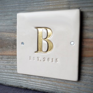 A white ceramic tile on a wood planter box (wedding centerpiece) with hand-stamped initial (painted gold) and Est. date.