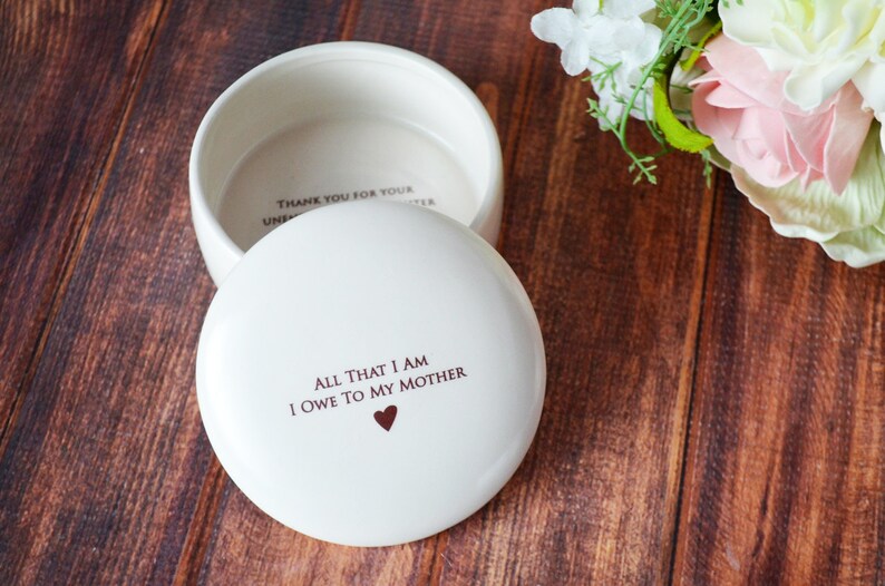 May include: White ceramic trinket box with a lid. The lid has the inscription "All that I am I owe to my mother" with a small heart symbol. The inside of the box has the inscription "Thank you for your unconditional love".