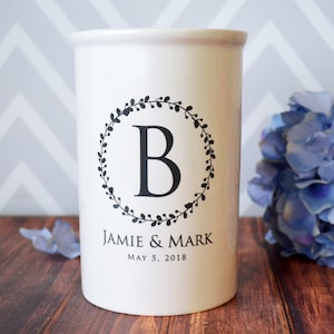 May include: White ceramic utensil holder with a black wreath design and the letter "B" in the center. The text "Jamie & Mark" and "May 5, 2018" is printed below the wreath.