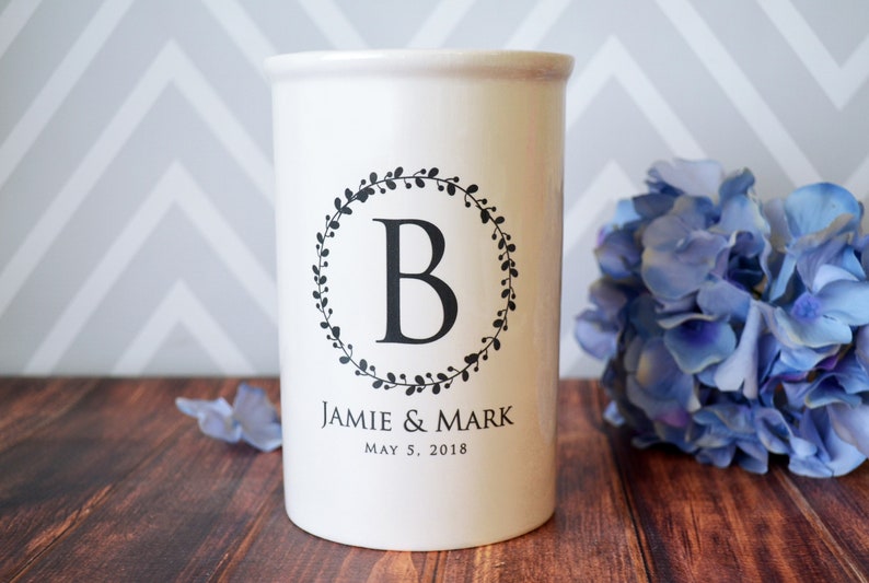 May include: White ceramic utensil holder with a black wreath design and the letter "B" in the center. The text "Jamie & Mark" and "May 5, 2018" is printed below the wreath.