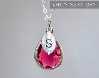 May include: A silver necklace with a teardrop-shaped pink crystal pendant and a small silver leaf charm with the letter "S" engraved on it.